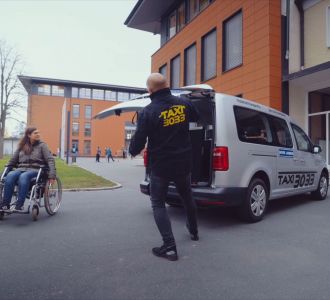 Frau im Rollstuhl vor einem Inklusionstaxi