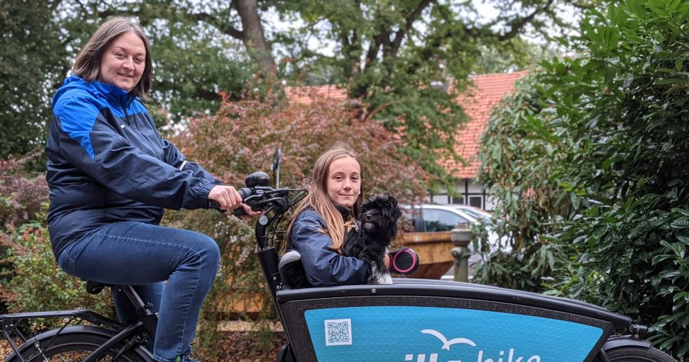 Eine Frau fährt ein milla-bike-Lastenrad mit einem Mädchen und einem Hund im Lastenkorb.