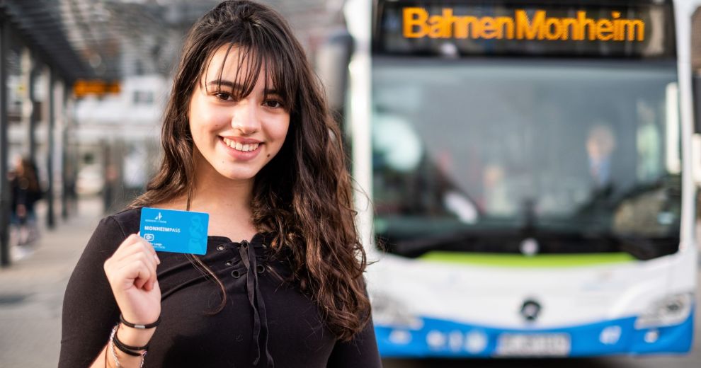 Eine junge Frau, die vor einem Bus steht und den Monheimpass in die Kamera hält.