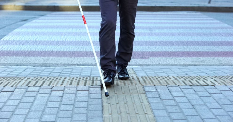 Sehbehinderte Person mit Blindenstock auf taktilen Fliesen.