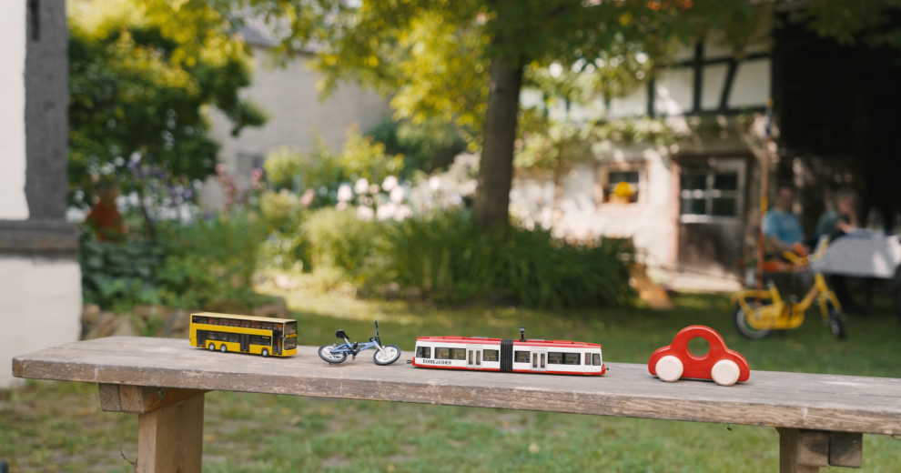 Spielzeugfiguren eines Busses, eines Fahrrads, eines Autos und eines Zuges auf einem Holztisch