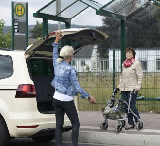 Ein wartender Fahrgast an einer Bushaltestelle wird vom Taxi abgeholt