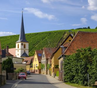 Dörfliche Siedlung mit Kirchturm und Weinbergen.