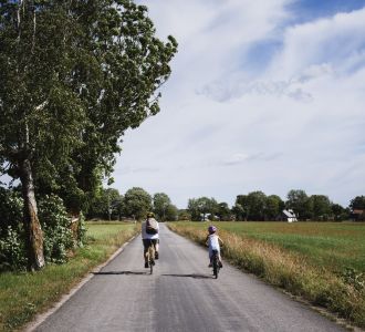 Vater und Tochter fahren mit dem Fahrrad auf einem Fahrradweg zwischen den Feldern einer Siedlung.