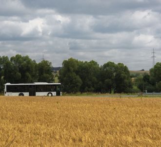 Landwirtschaftlich geprägte Landschaft mit vorbeifahrenem Bus.