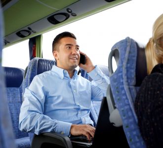 Mann mit Smartphone und Laptop im Bus.
